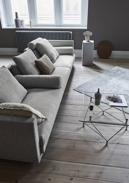 Cocoon Sofa by Eilersen at Trade Source Furniture in a spacious living room, styled in grey fabric with multiple cushions and a glass coffee table.
