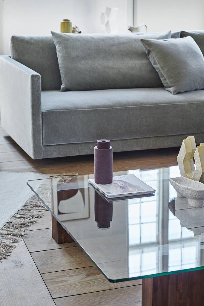 Close-up of blue Eilersen Drop Sofa armrest and cushions, paired with a glass coffee table and decorative accents.