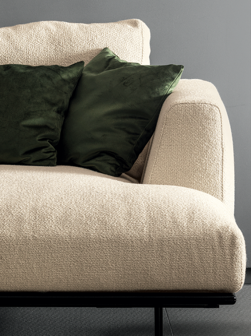 A close-up of a modern beige fabric sofa with textured upholstery, accented by dark green velvet cushions, showcasing contemporary furniture design.