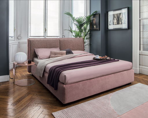 Elegant bedroom with pink upholstered bed featuring a high headboard, surrounded by modern decor, natural light, and stylish accents.