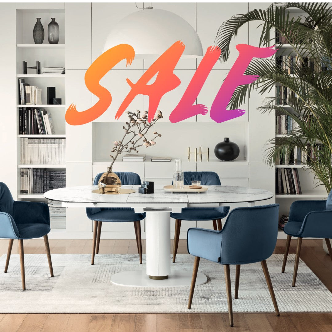 A modern dining room with a white marble table, blue upholstered chairs, and stylish decor, featuring a boldSALE" overlay for Labor Day Furniture Sale.