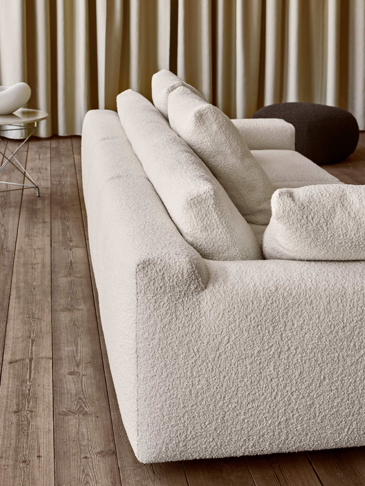 A cozy living room with a plush, textured white sofa, wooden flooring, and neutral curtains, showcasing stylish and comfortable home decor.