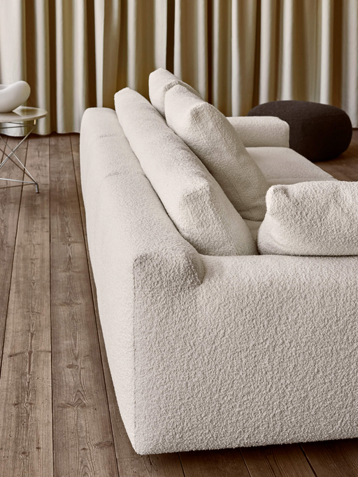 A cozy living room with a plush, textured white sofa, wooden flooring, and neutral curtains, showcasing stylish and comfortable home decor.