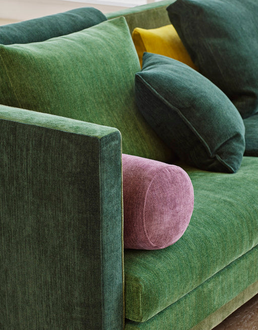 A vibrant green velvet sofa with colorful accent pillows in dark green, yellow, and pink, showcasing trendy 2024 interior color styles.