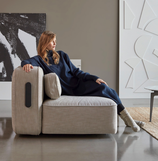 A woman relaxing on a modern, beige sofa with built-in massage features in a stylish, contemporary living room with abstract wall art.
