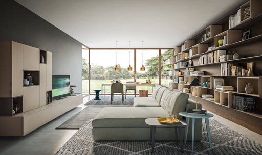 A modern, minimalist living room featuring a large wall-mounted modular bookshelf, neutral-toned sofa, and expansive glass windows with scenic outdoor views.