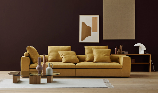 A modern home office or living room setup with a mustard yellow sofa, decorative pillows, abstract wall art, and a sleek glass coffee table, illustrating the balance of life and work from home in the new normal.