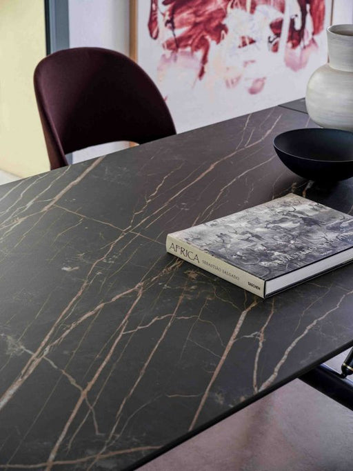 A sleek black marble dining table with gold veining, featuring a modern design, with a book titledAfrica" and decorative vases, in a contemporary interior.