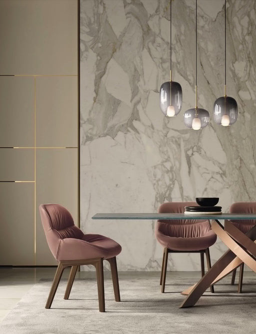 Elegant dining room with blush velvet chairs, modern glass-top table, and contemporary pendant lighting against a marble accent wall, showcasing new Bontempi Casa furniture designs for 2024.