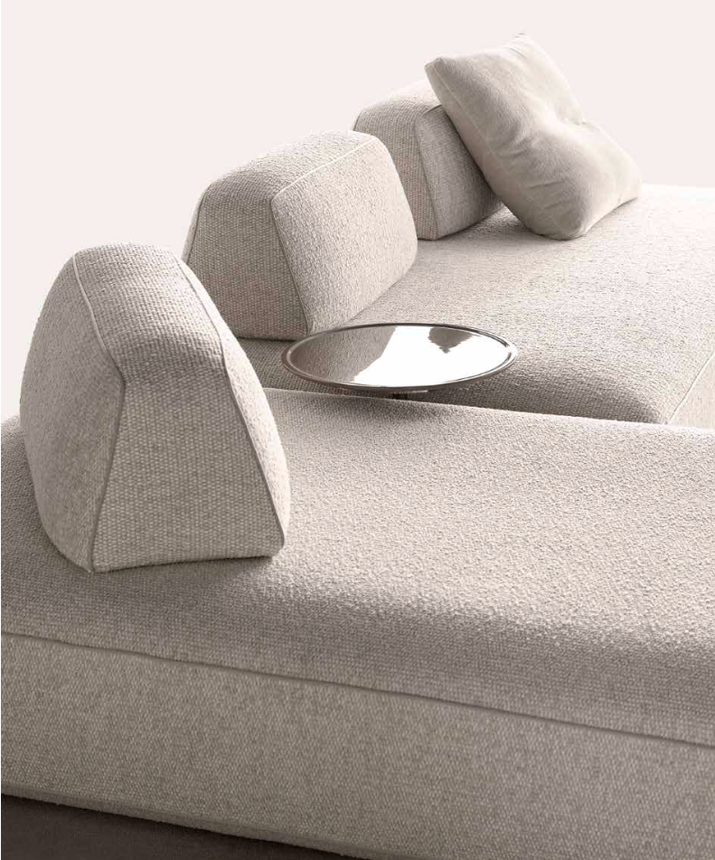 Minimalist beige sofa with movable backrests and matching cushions, designed for open interior spaces and flexible seating arrangements.