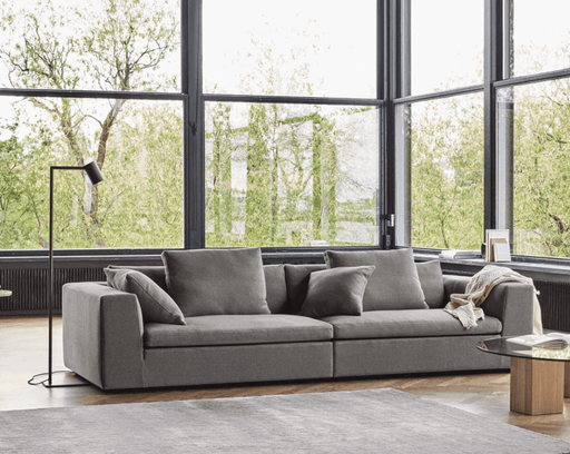Modern gray Eilersen quick ship sofa with plush cushions in a bright living room featuring large floor-to-ceiling windows and minimalist decor.