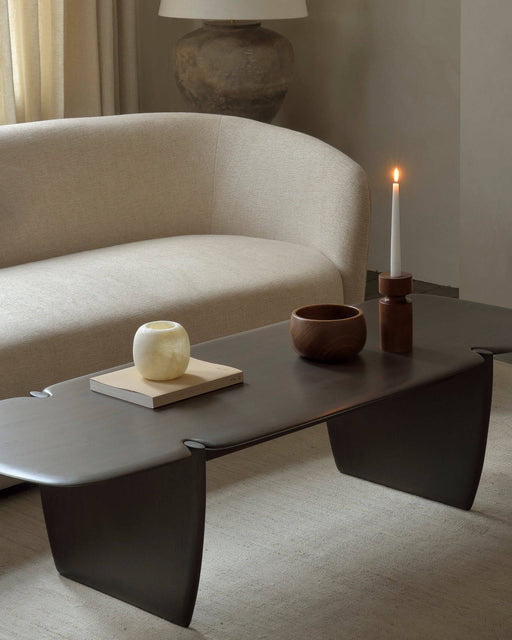 A minimalist living room with a beige upholstered sofa, modern black coffee table, decorative vases, and a lit candle, showcasing contemporary furniture and interior design.
