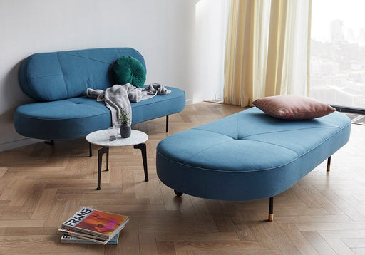 Modern blue sofa collection with sleek, curved design and minimalist black legs, featuring a matching ottoman and cozy throw blanket in a stylish living room setting.