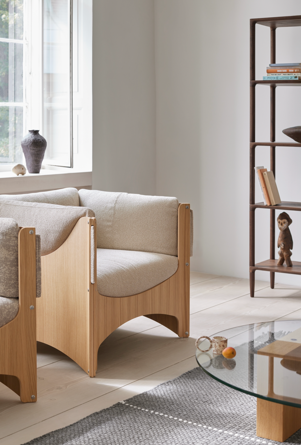 A minimalist living room featuring a modern Danish sofa with wooden frame and beige upholstery, complemented by a dark wood bookshelf and decorative ceramics, emphasizing Scandinavian design and craftsmanship.