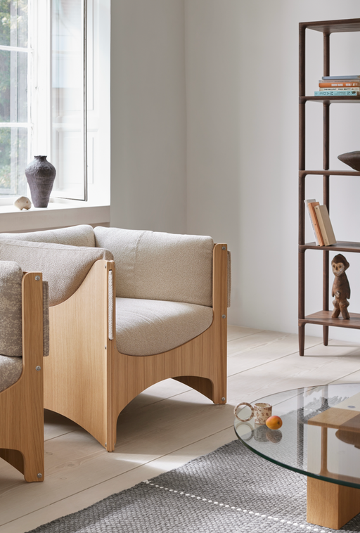 A minimalist living room featuring a modern Danish sofa with wooden frame and beige upholstery, complemented by a dark wood bookshelf and decorative ceramics, emphasizing Scandinavian design and craftsmanship.