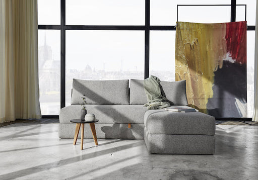 Modern grey sofa bed in a stylish urban living room with large windows, ideal for hosting guests during summer in the city.