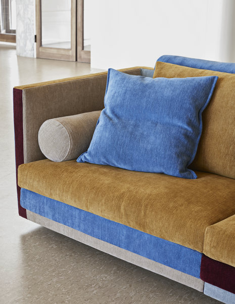 A modern sofa featuring a vibrant color palette of blue, mustard yellow, beige, and burgundy, showcasing interior design trends for 2026.