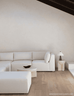A modern light beige sectional sofa with matching ottomans in a minimalist, warm-toned living room setting with light wood flooring and a textured cream wall.