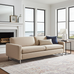 Beige sofa in a living room with large windows and a fireplace.