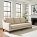 Beige sofa in a living room with large windows and a fireplace.