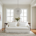 White sofa in a living room with large windows and a decorative chandelier.