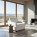 Modern living room with a white armchair, wooden side table, and large windows overlooking a scenic view.