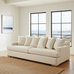 Beige sofa with several cushions and pillows in a room with large windows and a view of the ocean.