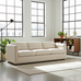 Beige sofa in a modern living room with large windows and a wooden bookshelf.