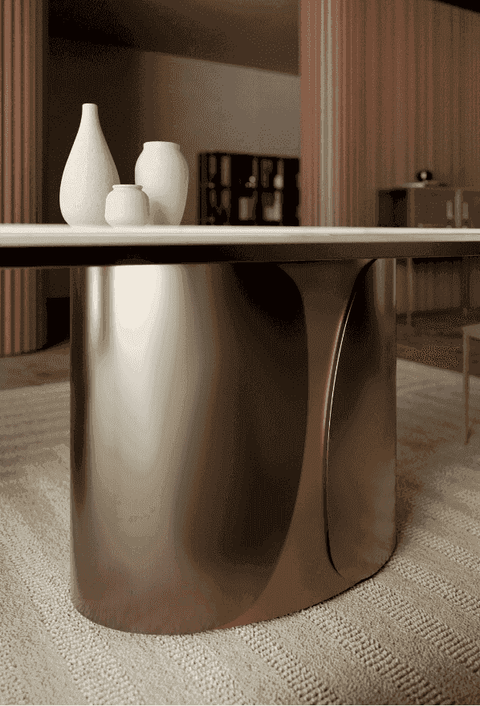 Close-up of the marble dining table with a gold curved base, minimalist white vases, and a warm ambient background