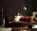 Woman sitting on a brown sofa in a dimly lit room with a large floor lamp.